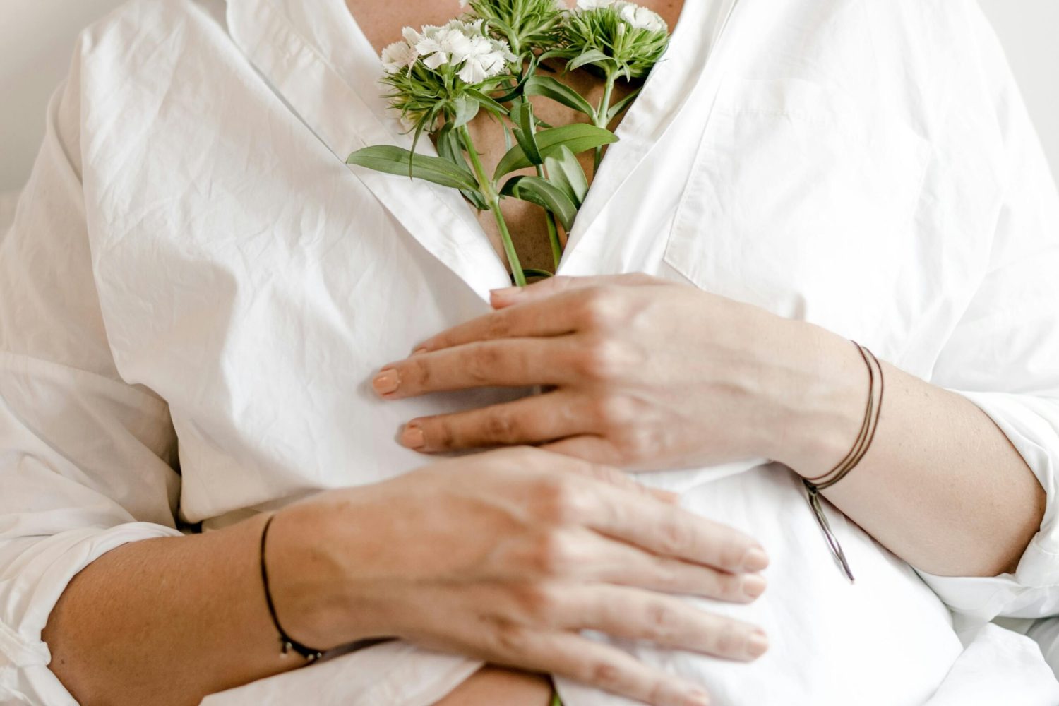 Image of pregnant women in white shirt holding white flowers against herself